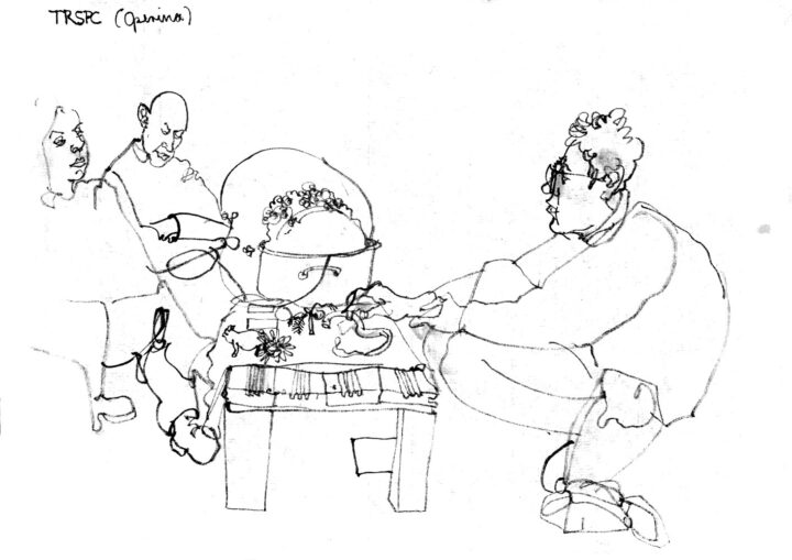 Inkdrawing of a perfomance: A man arranges different objects on a low table with a tablecloth, that serves as stage. Aside of the cloth is a big pot, soap-bubbles spill out of it in bulky shapes. On the left is the audience, two people sitting on chairs are dipicted.